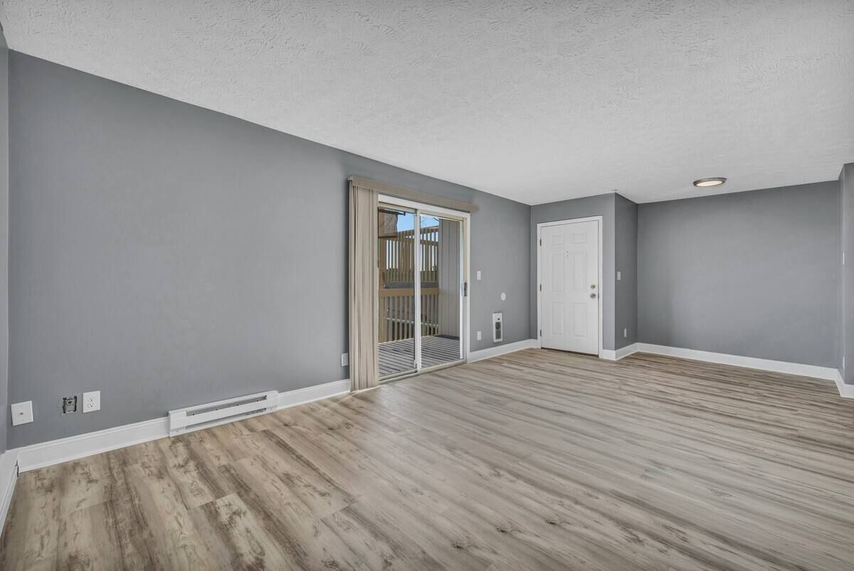 An empty living room with grey walls, a sliding glass door and wood-look flooring